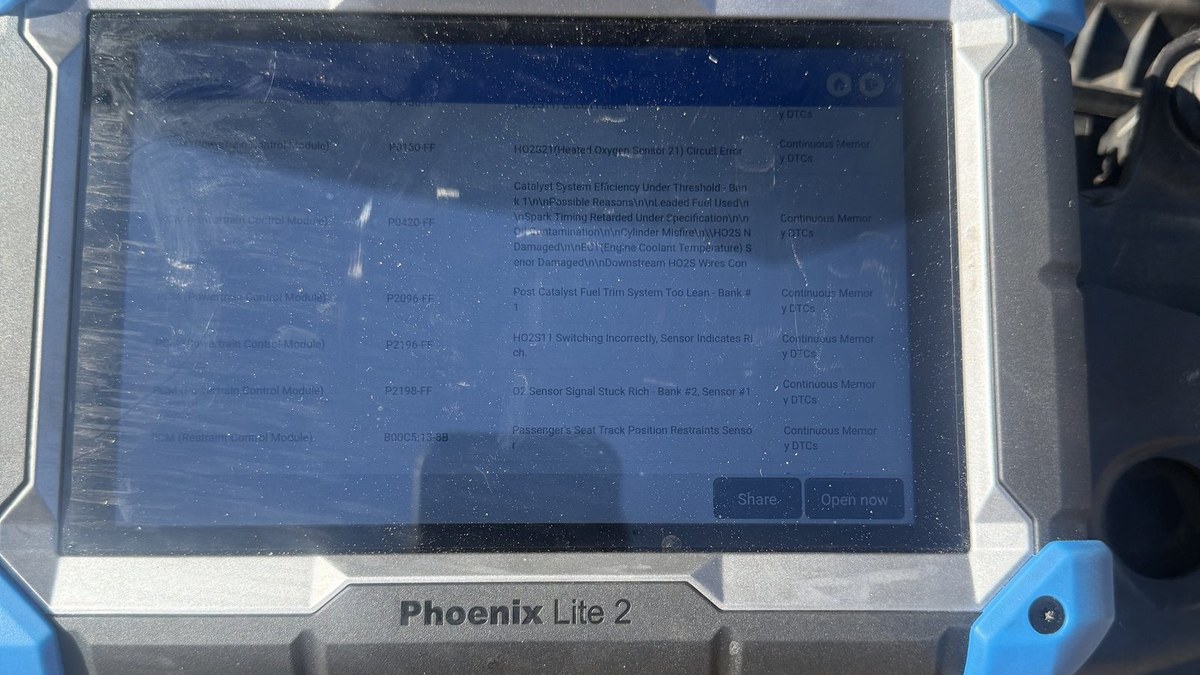 Topdon scan tool on a front bumper listing stored engine and module codes during a mobile diagnostic call