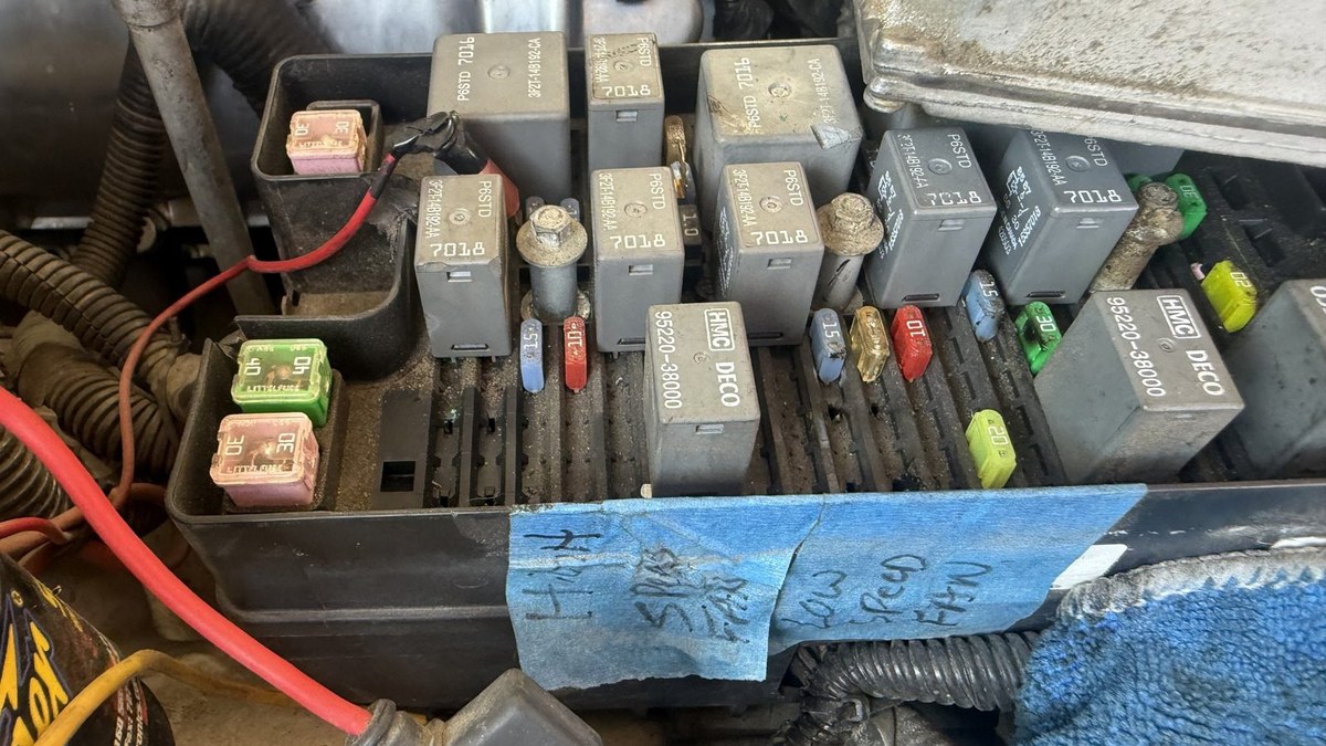 Underhood fuse and relay box open during a cooling fan circuit test, with the tech’s notes taped to the box