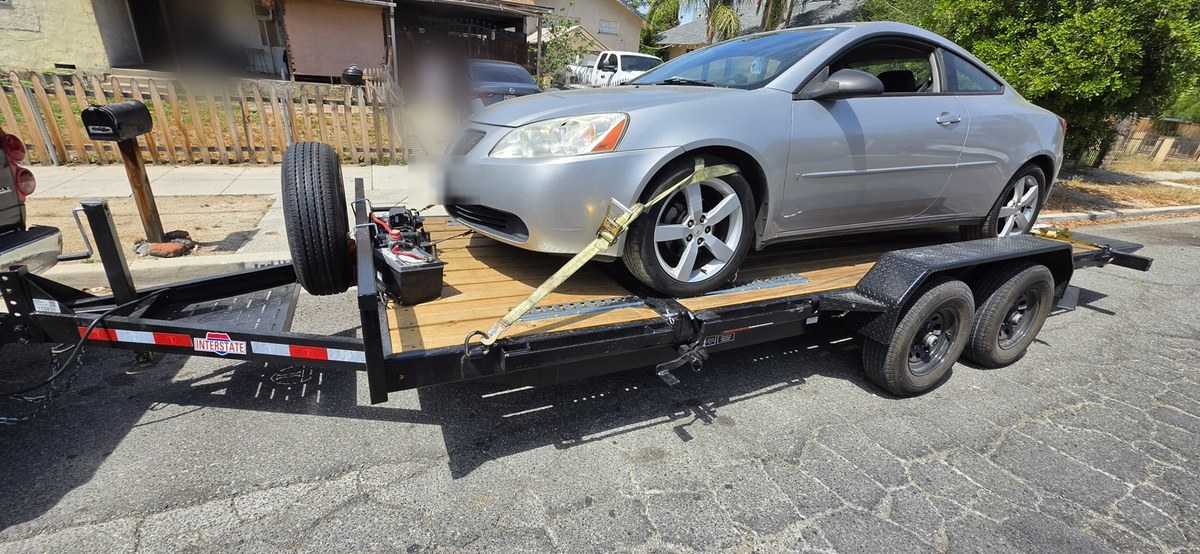 Silver Pontiac G6 coupe strapped down on a flatbed car trailer at the curb, ready to tow