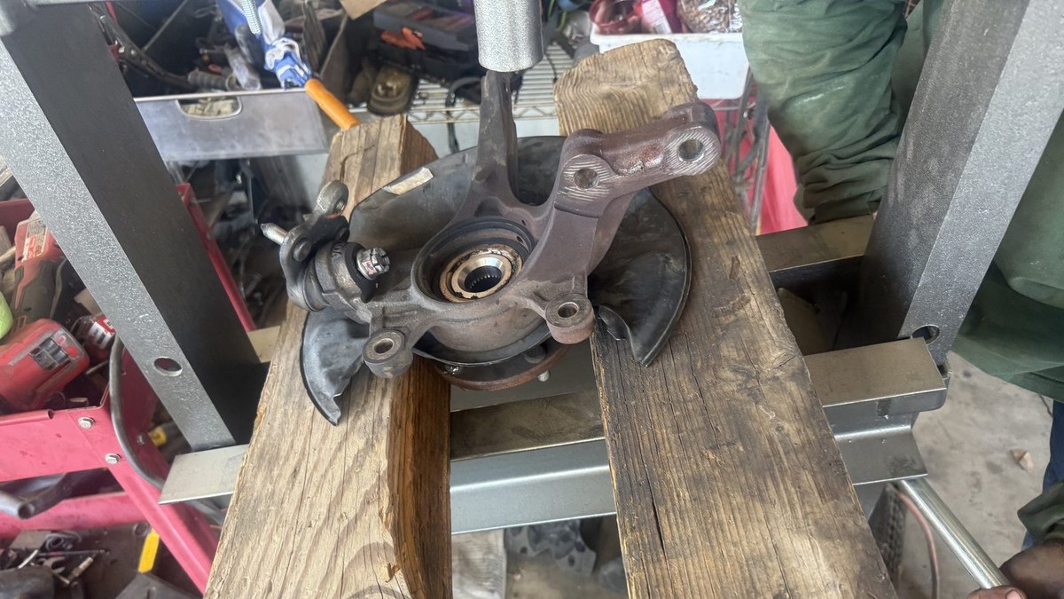 Steering knuckle and wheel hub set on wood blocks in the shop press, ready to press out the bearing