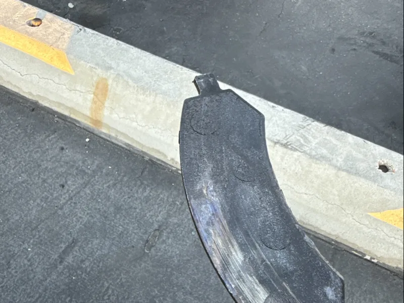 Worn-out brake pad held up in a parking lot after a brake job