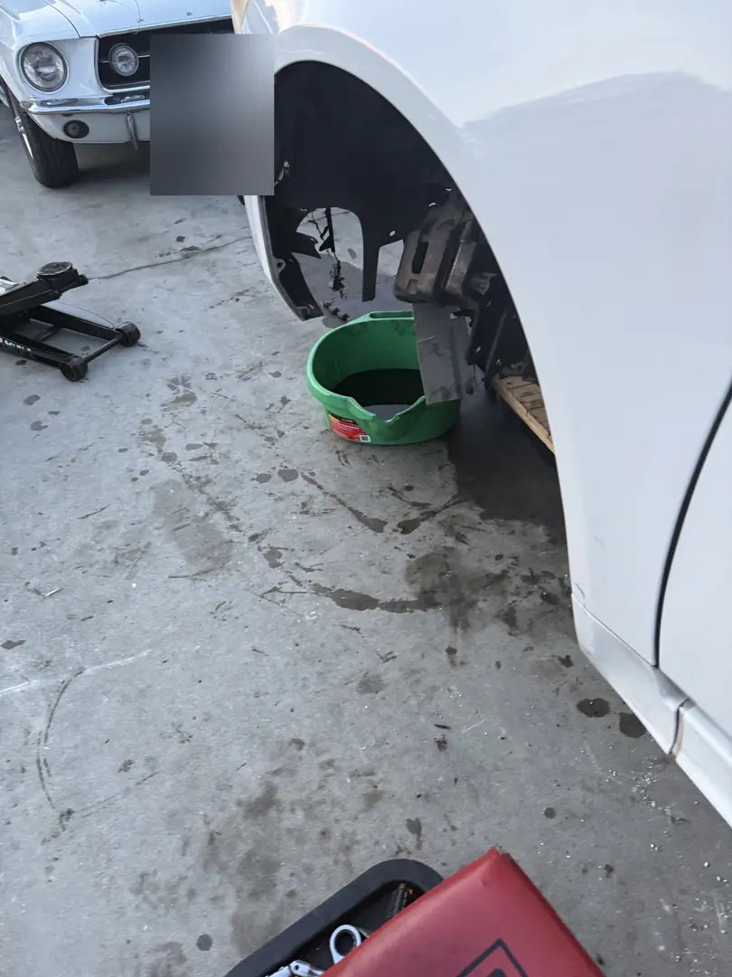 The front wheel well of a white classic Mustang with the wheel off on jack stands