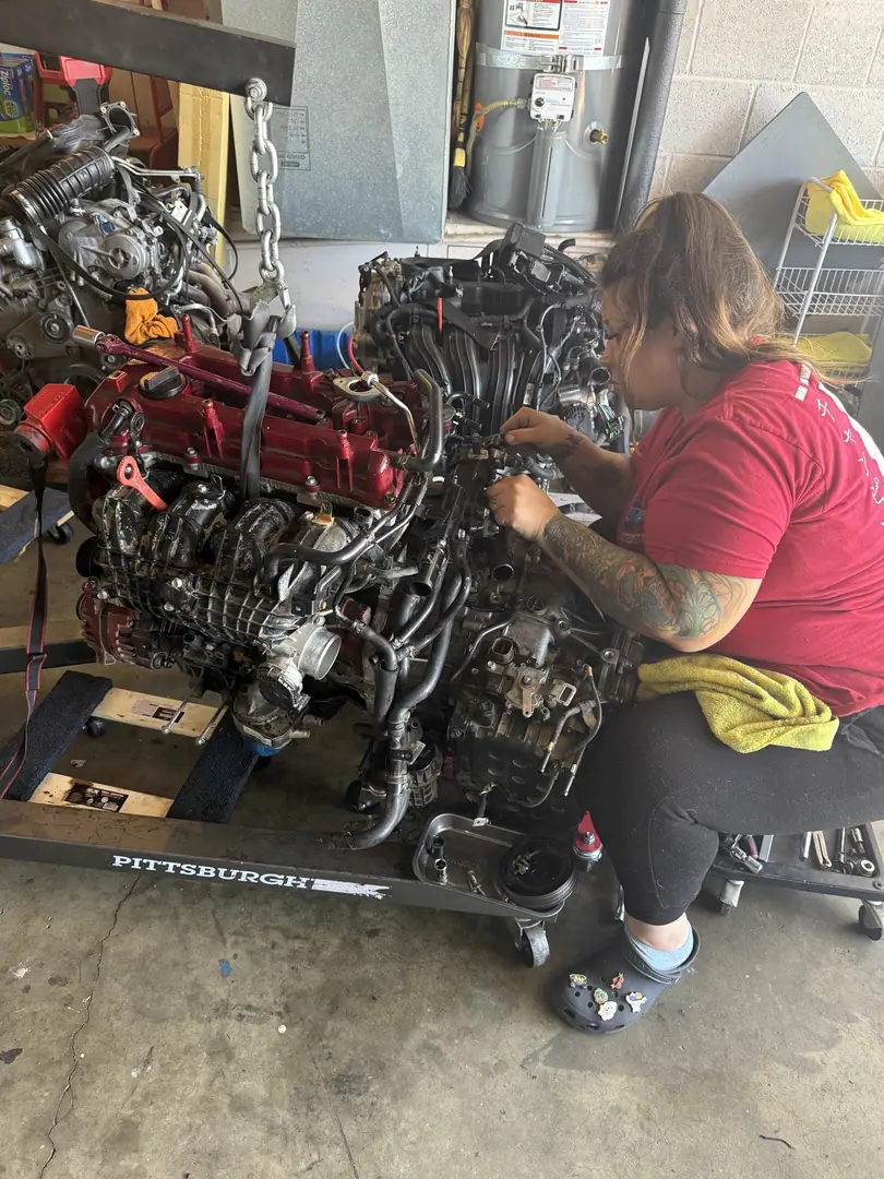 A mechanic working on an engine mounted on a stand dolly in a garage