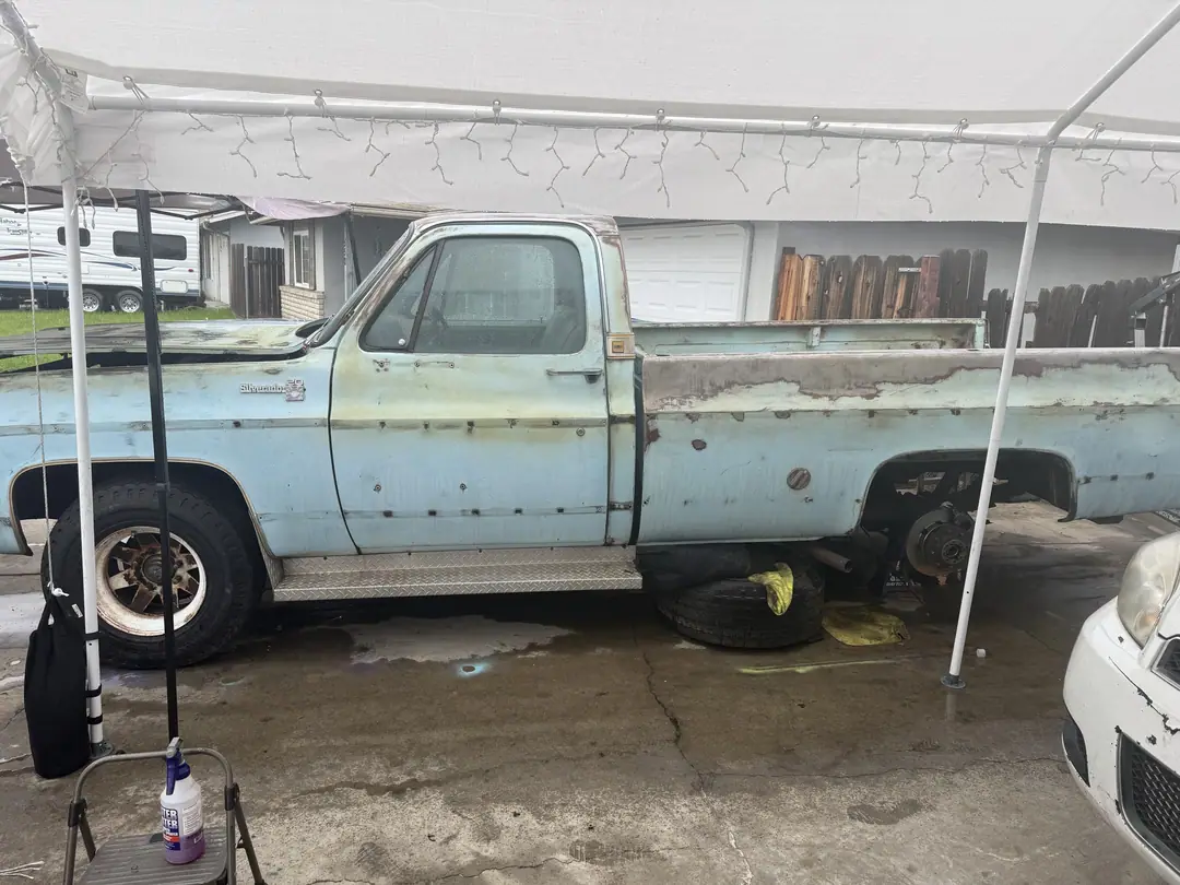 A pale blue square-body Chevy pickup parked under a white canopy in a driveway