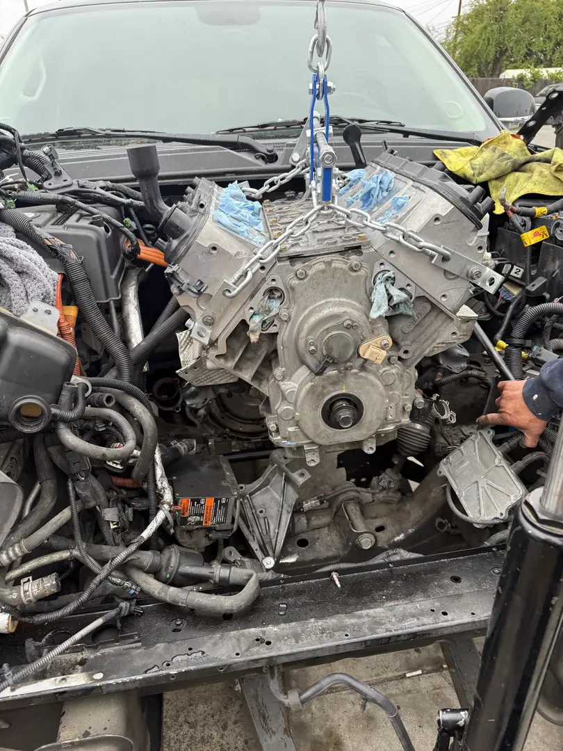 An LS V8 hanging from a hoist chain over the engine bay of a GM truck