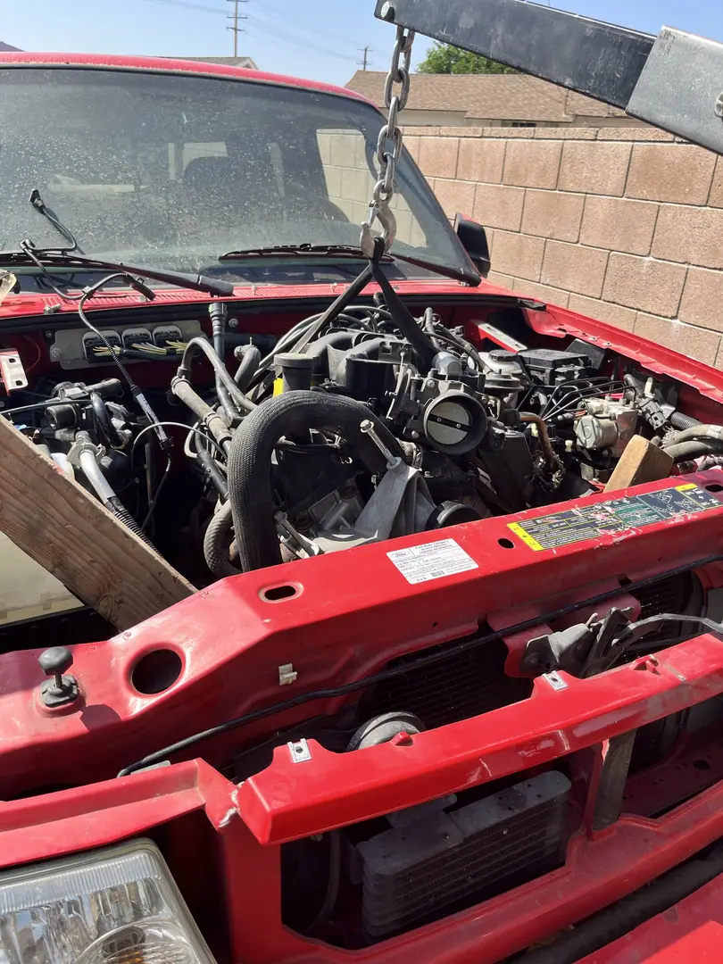 The engine bay of a red Ford Ranger with a hoist chain attached to the engine