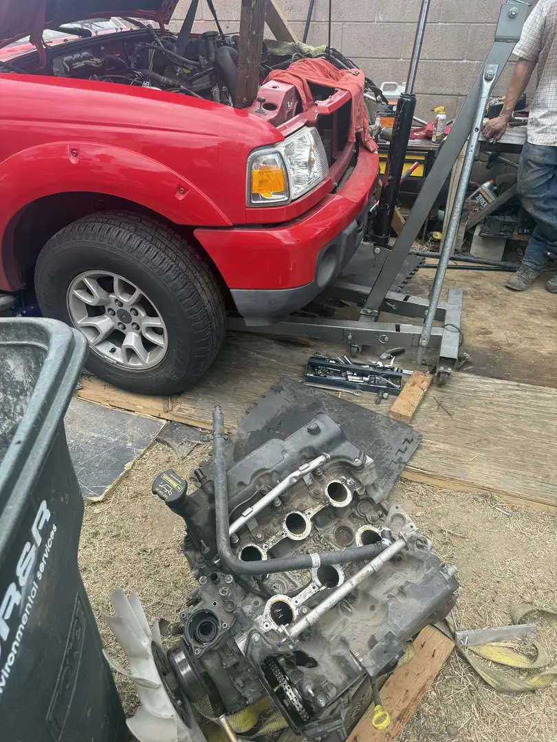 A red Ford Ranger with the hood off and an engine hoist beside it, the old engine on the ground