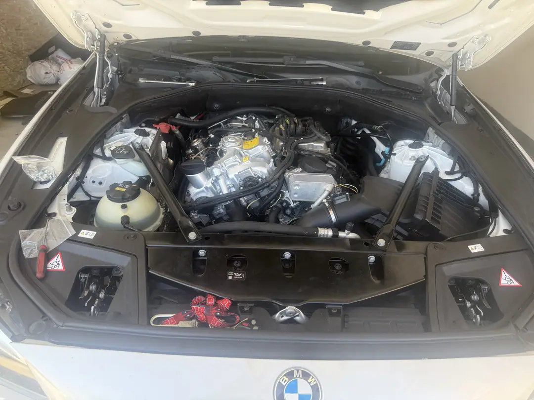 A white BMW 5 Series with the hood open and the engine covers removed, showing the turbo four cylinder engine