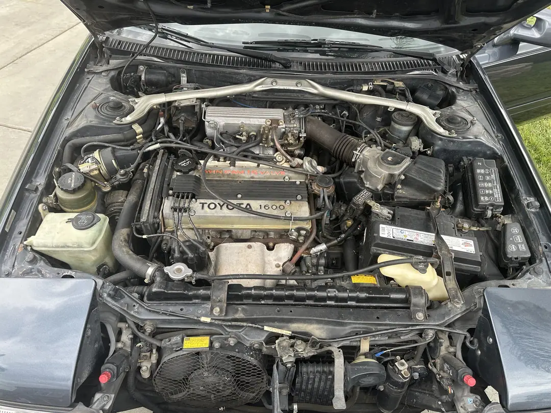 The engine bay of a gray Toyota with a 1600 four cylinder engine