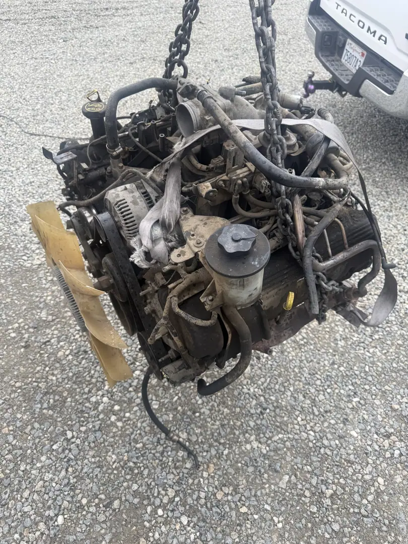 A V8 with wiring attached hanging from a hoist chain outside