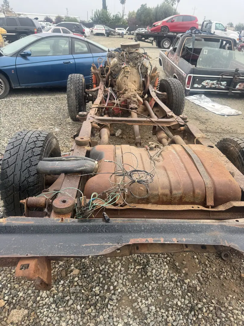 A truck chassis with the body removed showing the engine, frame rails and fuel tank on gravel
