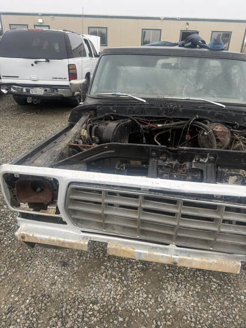A 1970s Ford pickup with the grille on and the engine bay stripped at a salvage yard
