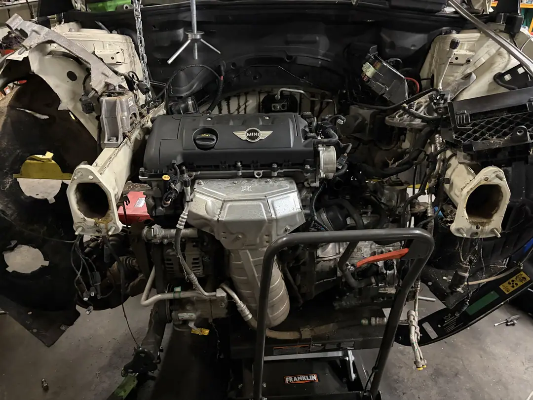 A Mini Cooper with the entire front end removed and the engine exposed in a shop bay