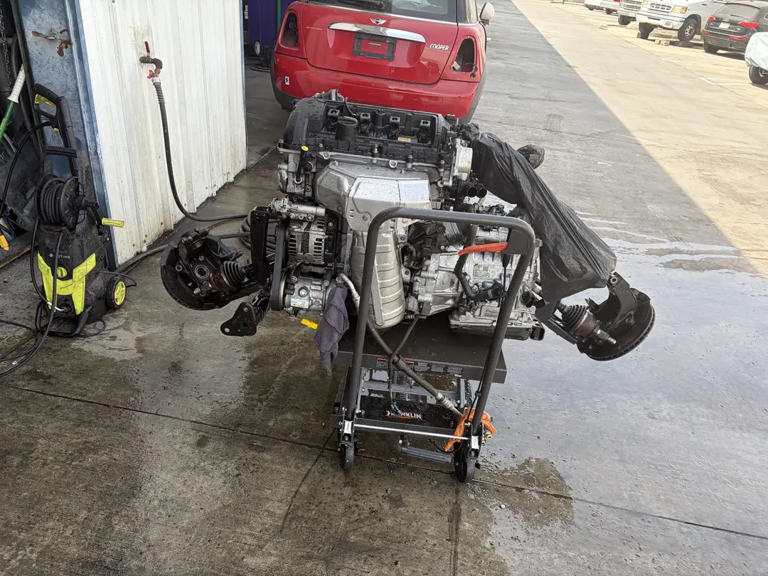 A Mini Cooper engine and transmission on a dolly outside the shop