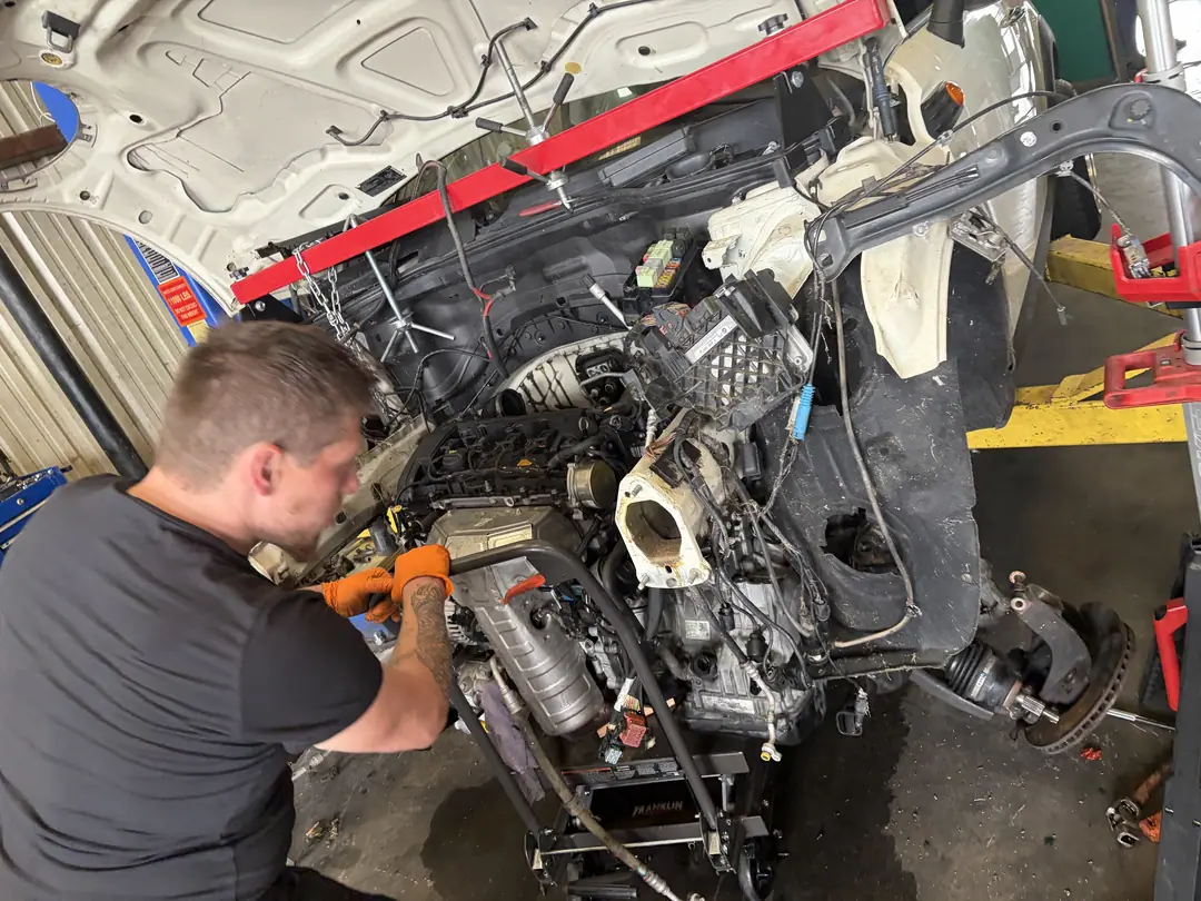 A mechanic working on the front of a Mini Cooper engine with the front end off
