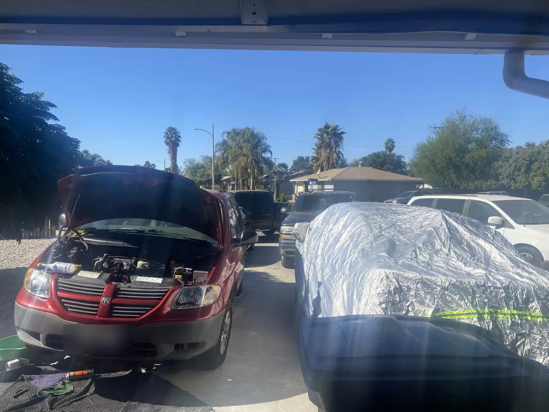 A red minivan with the hood up in a driveway next to a covered car, November 2024