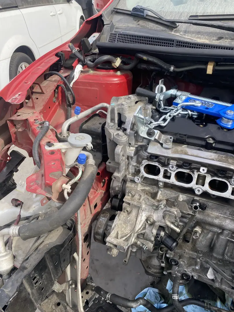A Nissan four cylinder engine chained to a blue lifting bracket, half out of a red car with the front clip removed