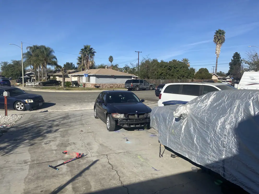 The driveway in January 2025 with a dark sedan and a covered car under blue sky