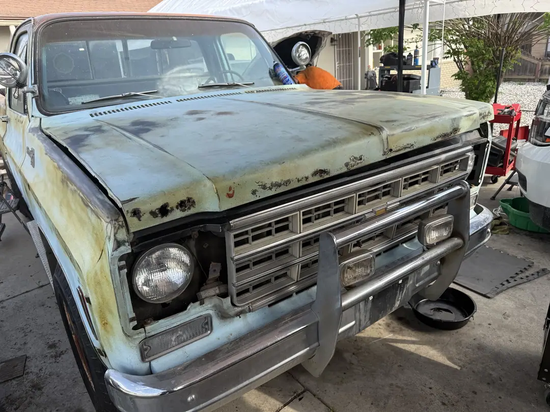 The front of a weathered pale blue square-body Chevy pickup with the hood closed
