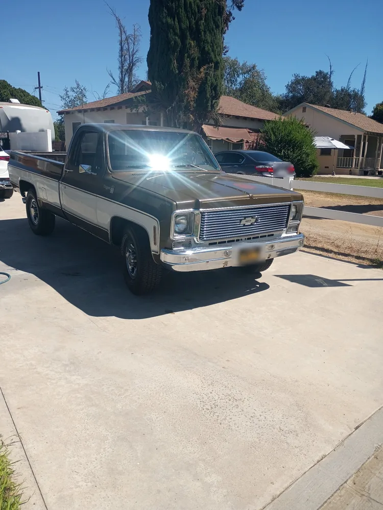 A brown and white 1976 Chevy Cheyenne pickup parked on a driveway on a sunny day