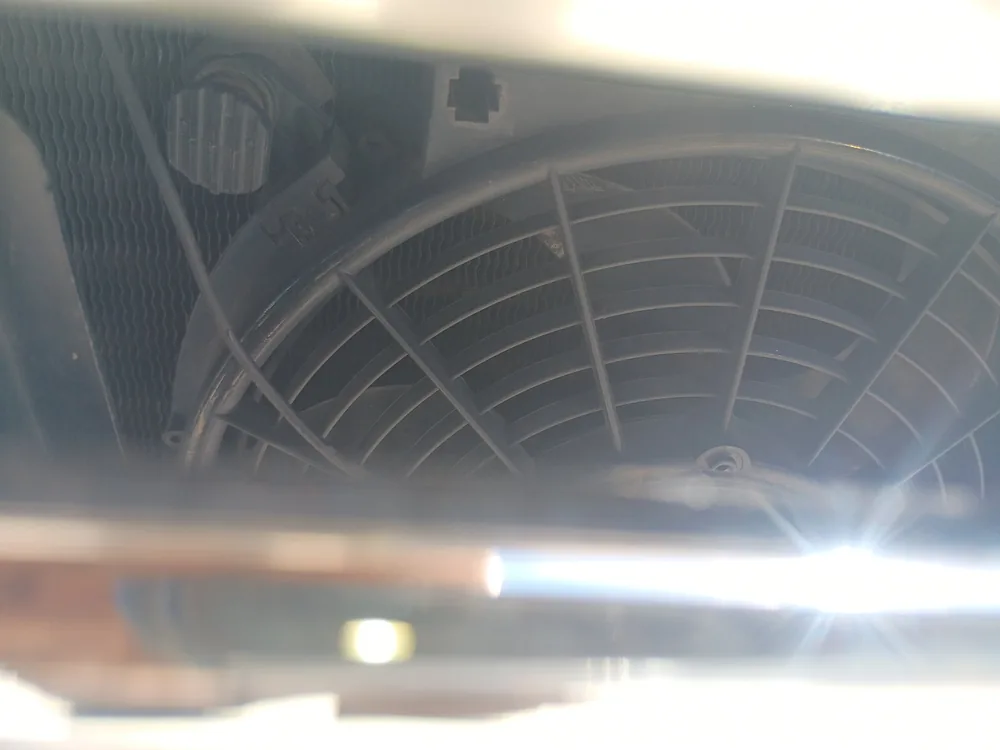 Electric cooling fan behind the radiator of a 1976 Chevy Cheyenne, with bright sun glare