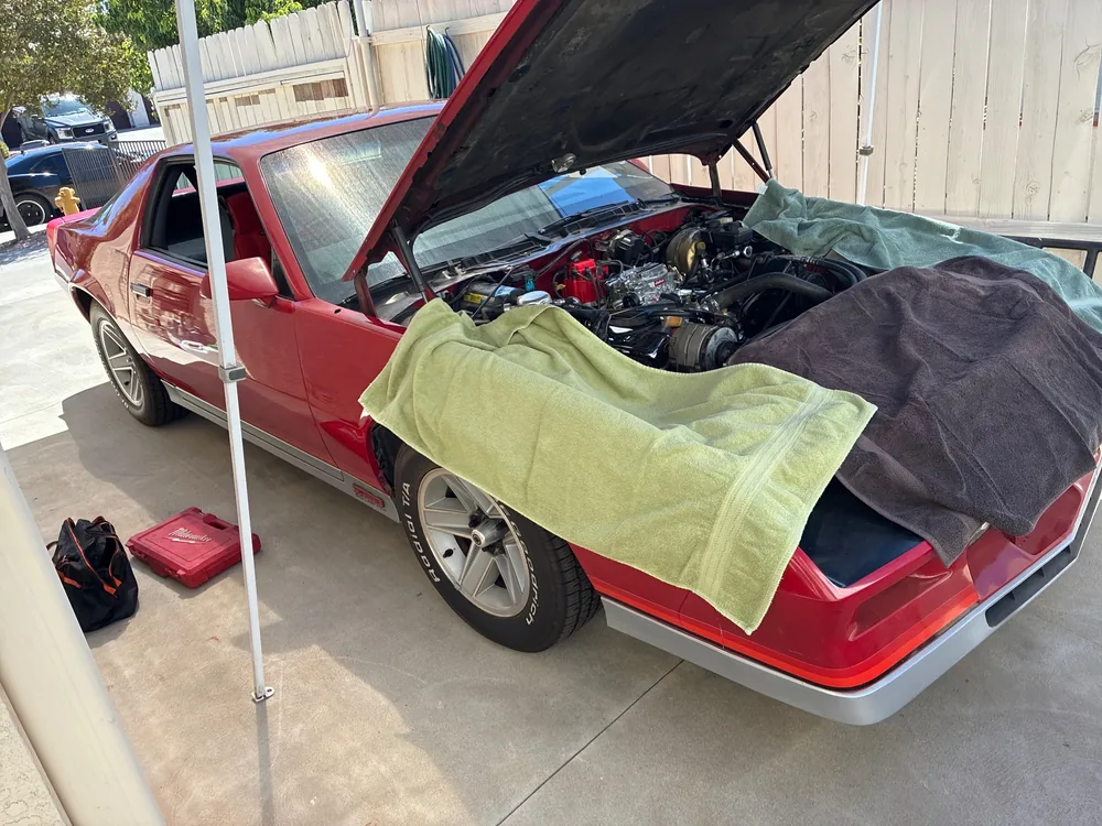 A red 1984 Camaro Z28 with the hood up and towels on the fenders in a driveway