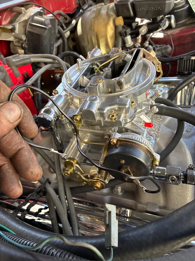 A new four barrel carburetor on a fresh intake manifold, a hand holding the wiring