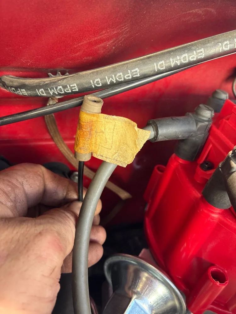 A hand holding a vacuum line near the red distributor cap of a Camaro