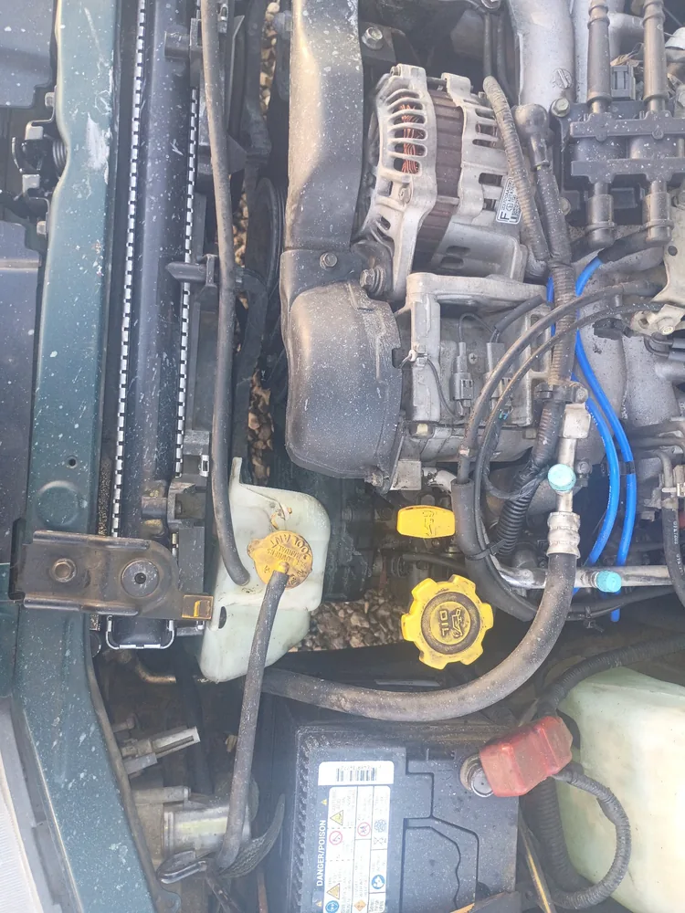 Engine bay of the 1998 Subaru Impreza after the cooling work, with the coolant overflow tank and battery in view