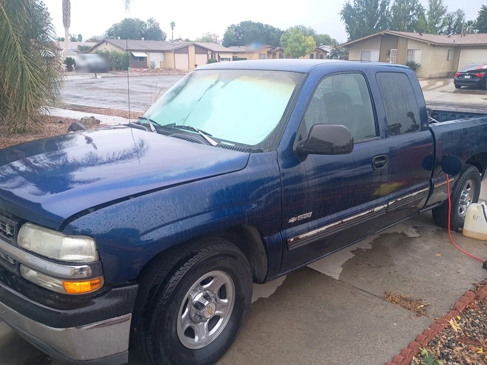 A blue 1999 Chevrolet Silverado in a driveway with a gas can and hose beside the bed