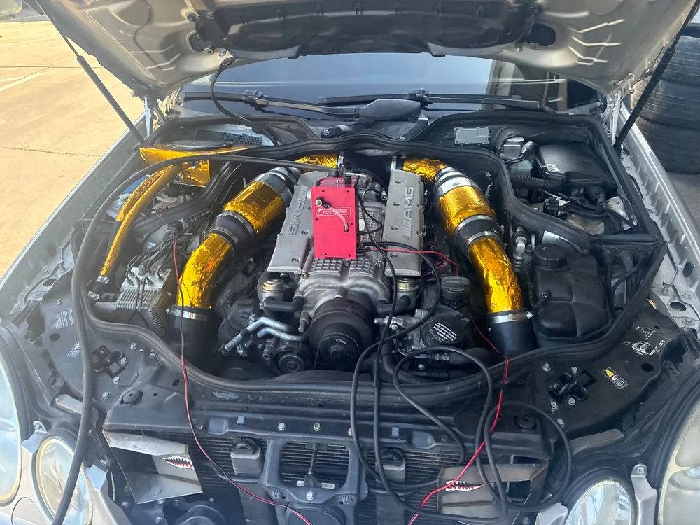 The supercharged 5.5 V8 in a 2005 Mercedes E55 AMG with a red smoke test machine sitting on the engine
