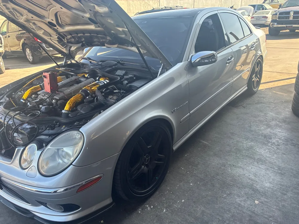 A silver 2005 Mercedes E55 AMG with the hood up and the smoke machine on the engine