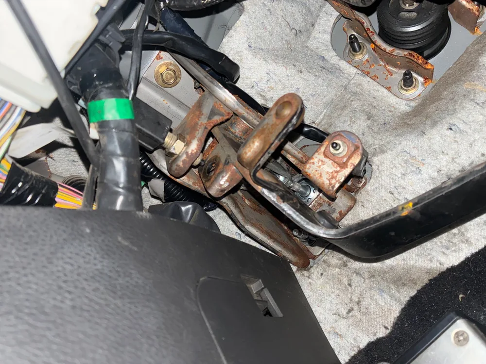 The pedal assembly under the dash of the 2005 Nissan 350Z with rusted brackets and the master cylinder pushrod