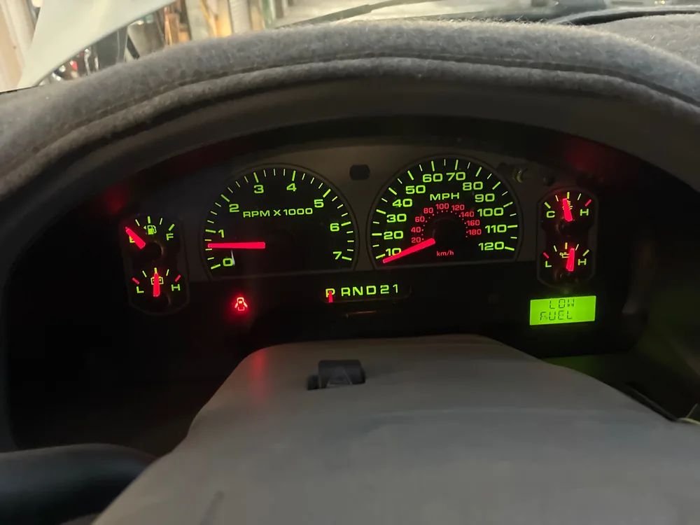 The lit instrument cluster of a 2006 Ford F-150 showing the gauges and a low fuel message