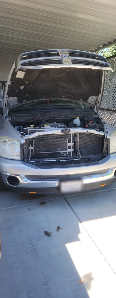 A silver 2007 Dodge Ram with the hood open under a carport and oil spots on the concrete below