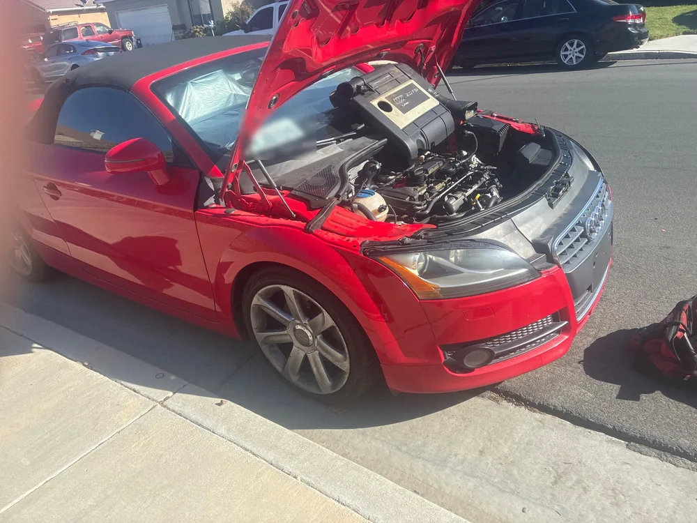 A red 2008 Audi TT roadster with the hood up at the curb for a fuel leak diagnosis