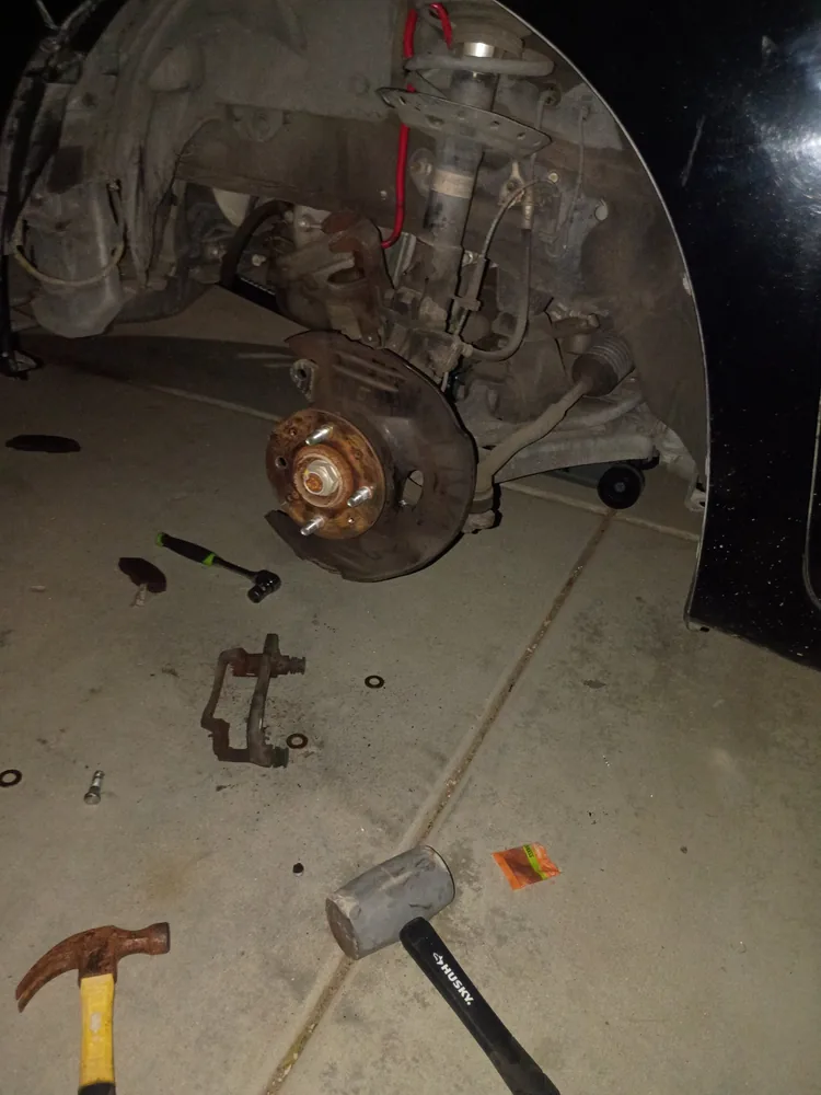 Front hub of a 2010 Honda Insight with the wheel and brake caliper removed in a driveway, hammers on the ground