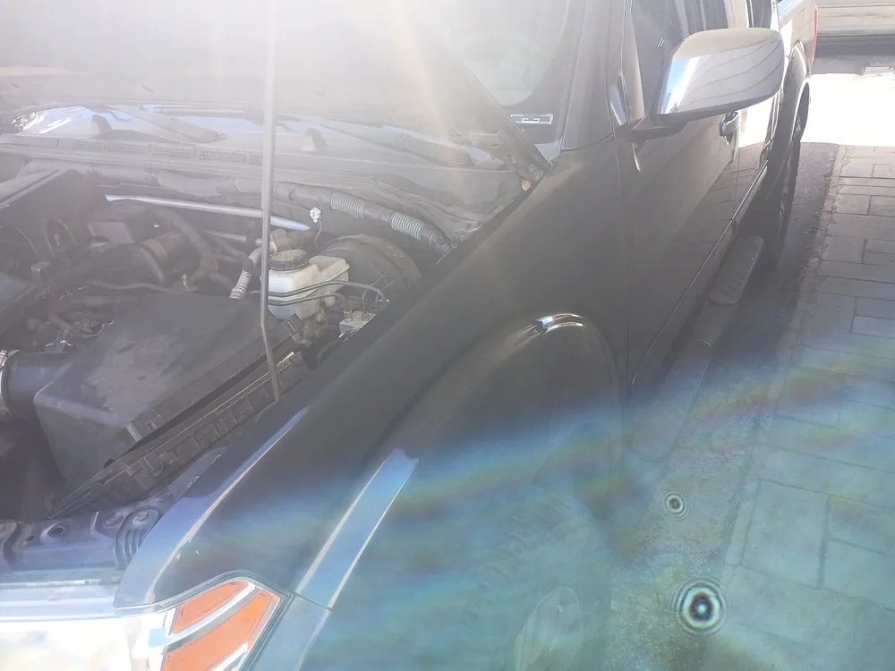 Engine bay of a gray 2010 Nissan Frontier with the hood open in a driveway