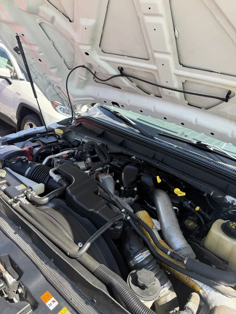 The diesel engine bay of a white 2011 Ford F-250 with the hood up on a dealer lot