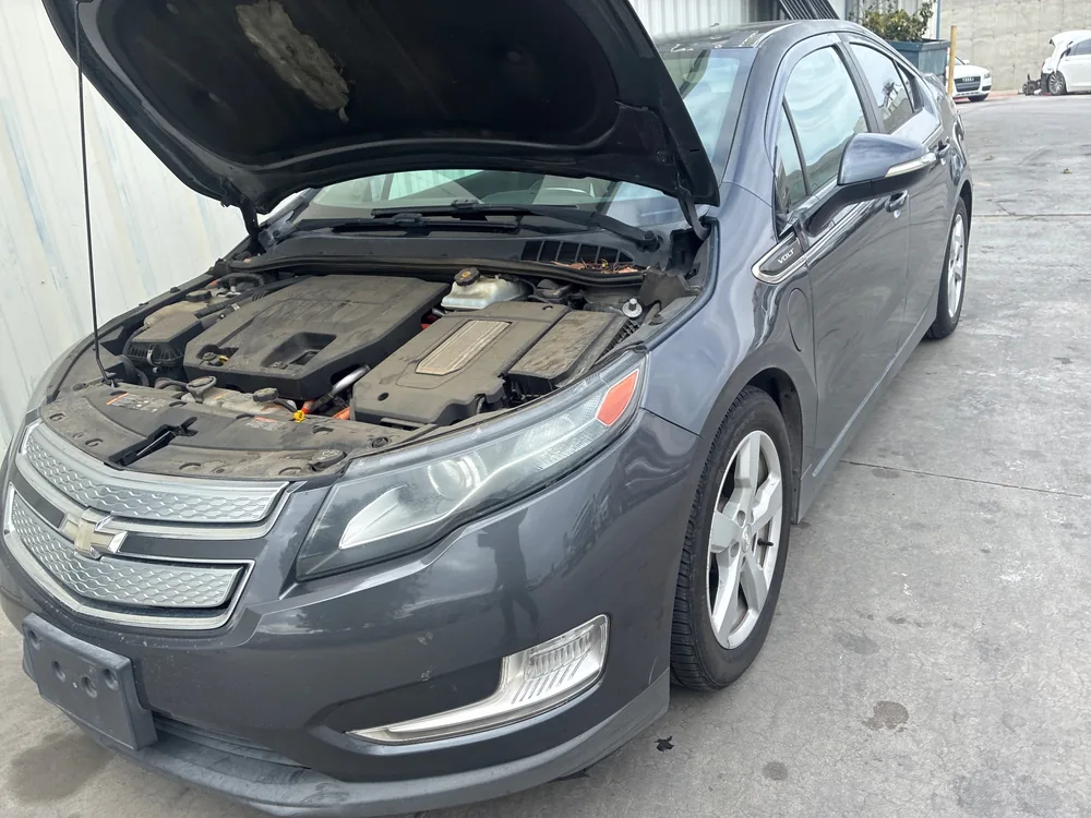 A gray 2013 Chevy Volt with the hood up beside a metal shop building