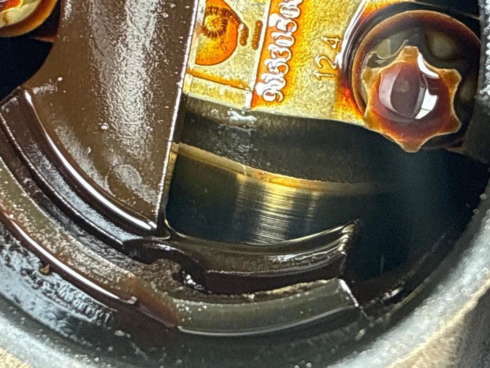 A close view inside the top of a 2013 Chevy Volt engine showing an oil covered camshaft lobe with wear on its surface