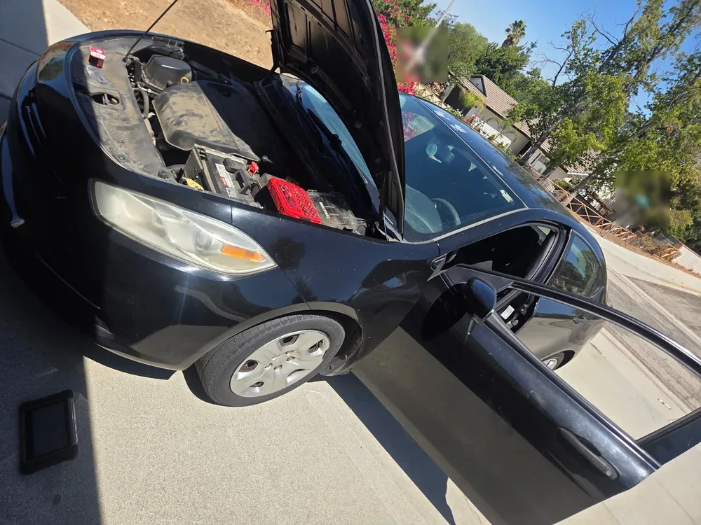 A black 2013 Dodge Dart with the hood up and a scan tool on the driveway during a Supercanic mobile visit in Riverside