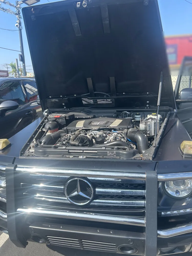 A black 2015 Mercedes G550 with the hood up on a dealer lot during a pre-purchase inspection