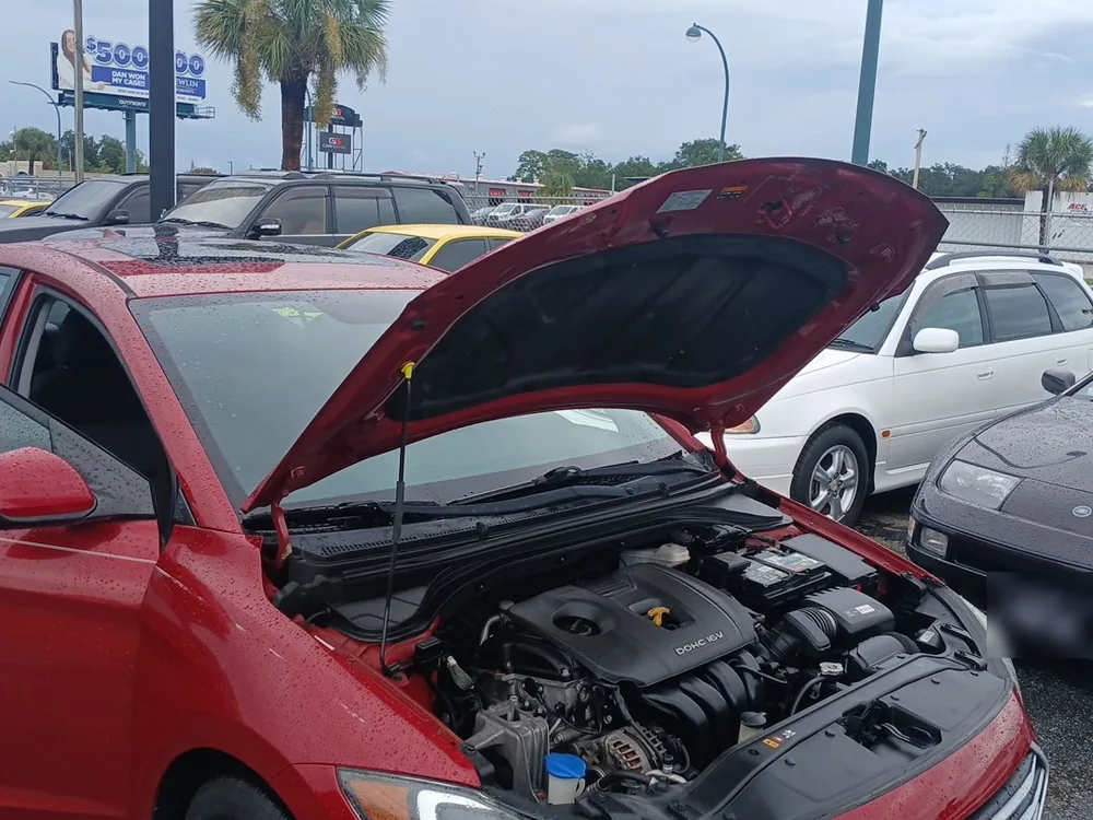 Engine bay of the red 2017 Hyundai Elantra with the hood up on a wet lot