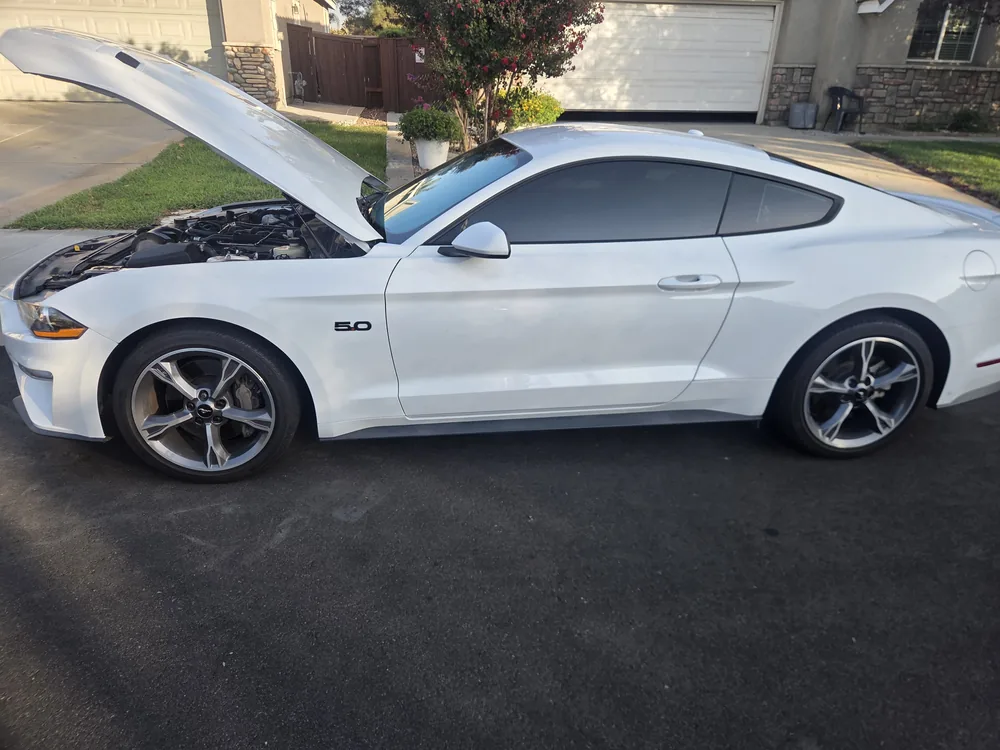 A white 2018 Ford Mustang GT parked in a Beaumont driveway with the hood up