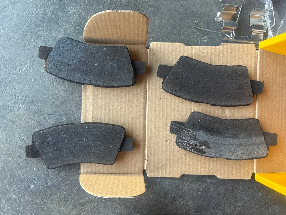 Four worn brake pads from the 2020 Hyundai Tucson laid out on a parts box, one with a badly damaged friction surface