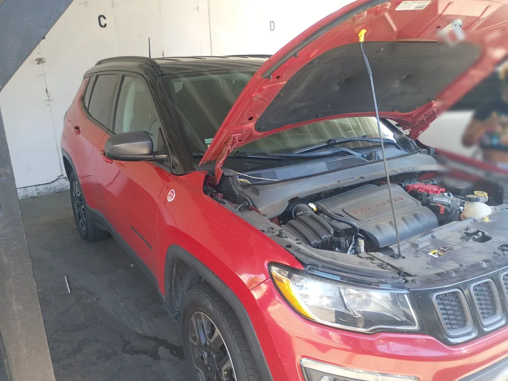 A red 2020 Jeep Compass with the hood up in a covered parking spot