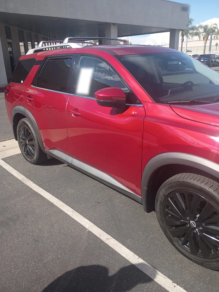 Driver side of a red 2022 Nissan Pathfinder on a dealer lot, showing doors, wheels and body lines