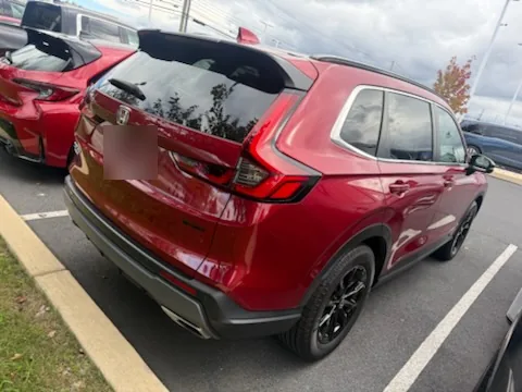 A red 2024 Honda CR-V Hybrid Sport-L seen from the rear corner on a dealer lot