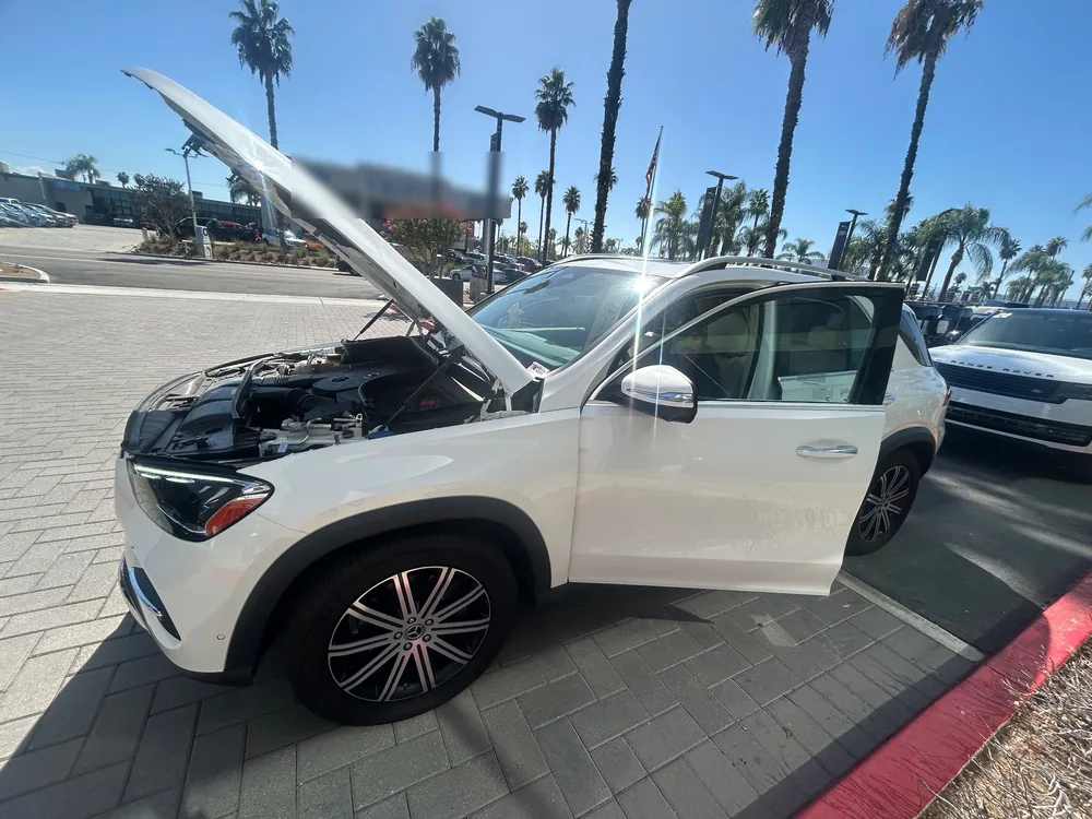 A white 2025 Mercedes GLE with the hood up and the driver door open on a dealer lot in Riverside